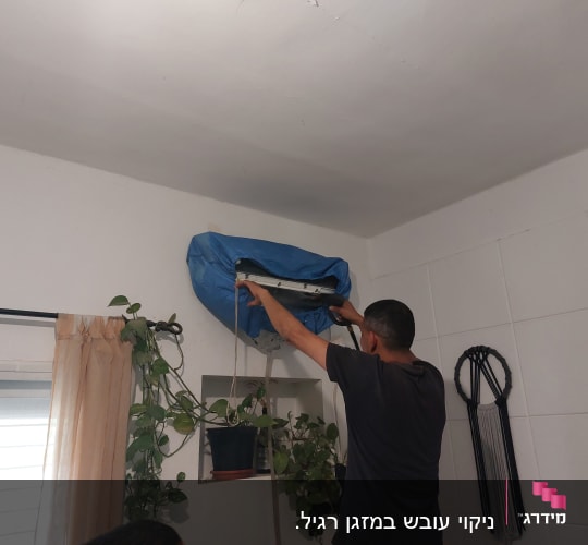 אדם מנקה מזגן עם כיסוי כחול על הקיר